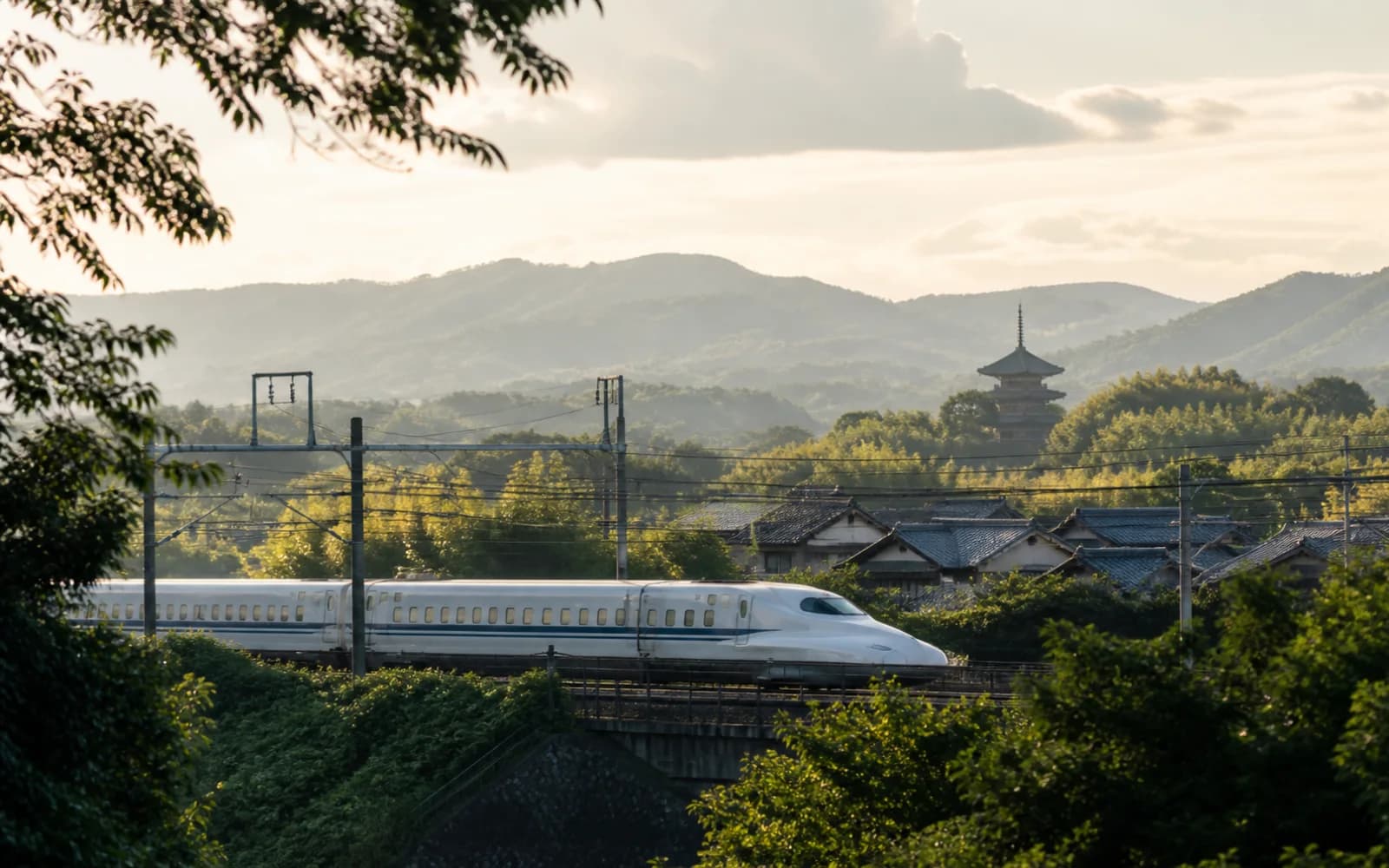 High-speed train crossing the green Kyoto countryside with a pagoda and mountains beyond.